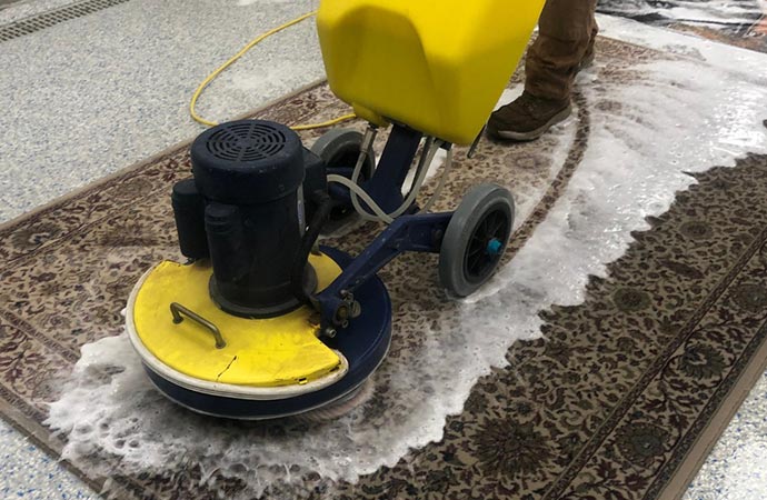 cleaning machine cleans a rug with rotating brushes and foam