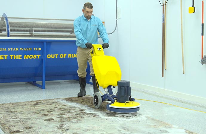 A professional rug cleaner is using a scrubber to deep clean a rug.